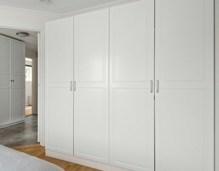 White wardrobes in a modern bedroom with wooden flooring.