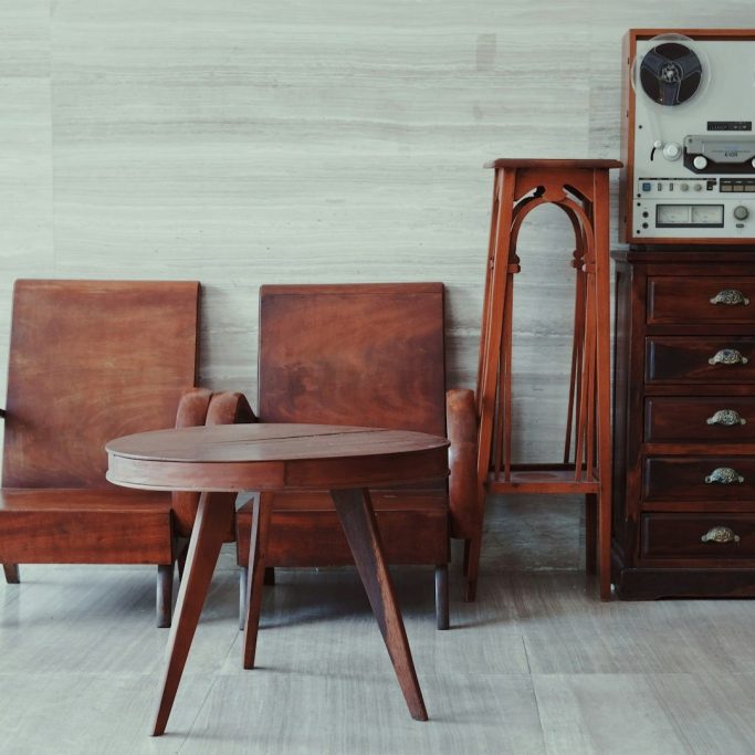 Vintage wooden chairs and a round table next to an antique record player and chest of drawers.