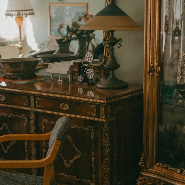 Antique wooden dresser and lamp beside a glass display cabinet in a vintage room.
