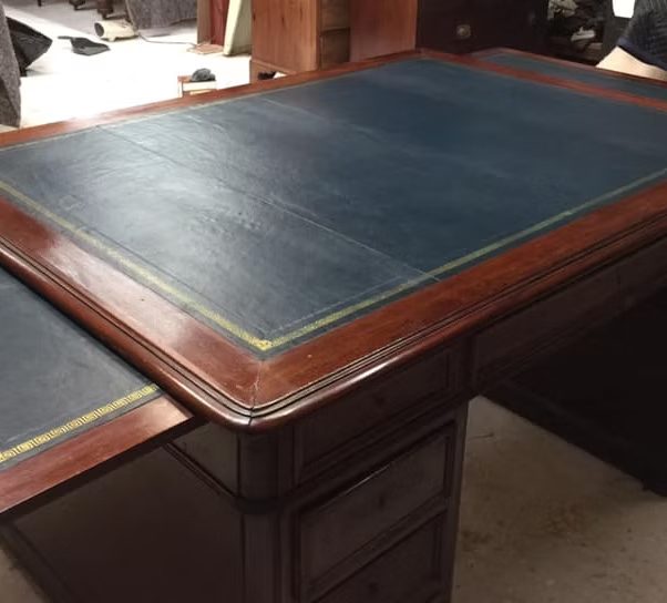 A wooden desk with a blue leather writing surface and a decorative green edge.