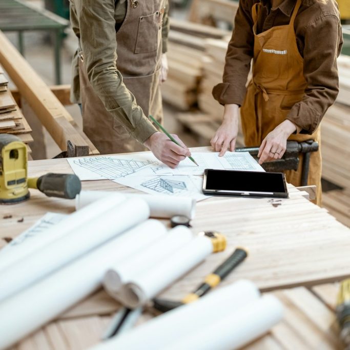 Two individuals reviewing construction plans at a workbench with tools and materials.