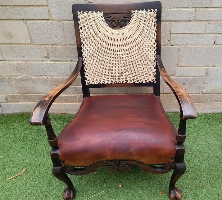 Antique chair with a woven back and brown leather seat on green grass.