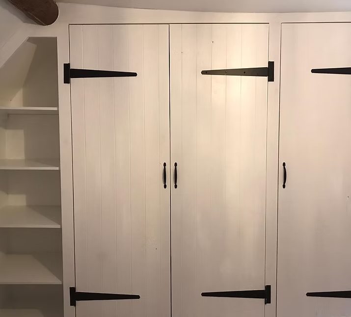 White wooden wardrobe with black handles, featuring black hinges and adjacent shelves.