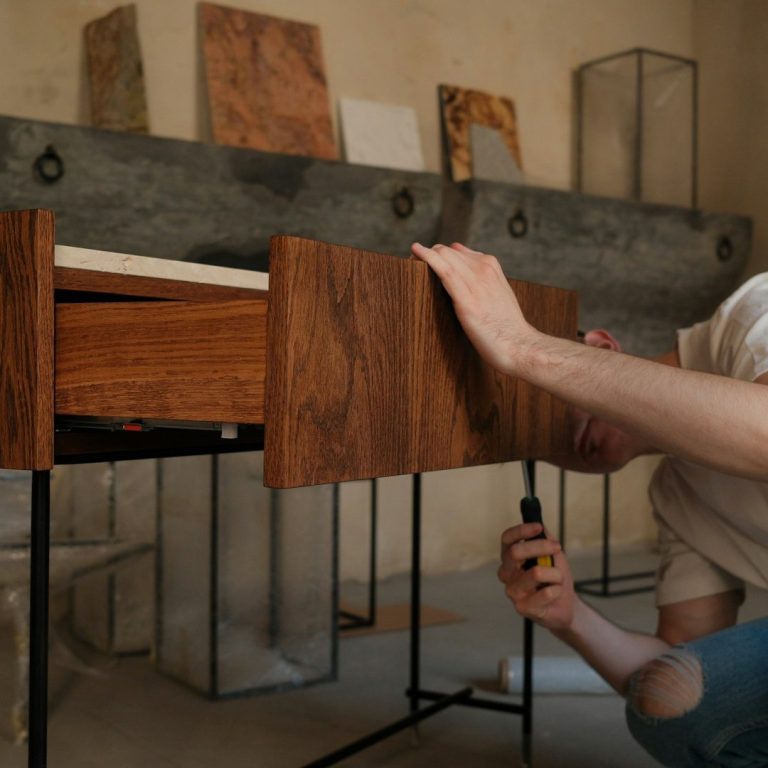 A person assembling a wooden cabinet with drawers in a minimalistic interior setting.
